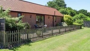 A brick building with a red-tiled roof, a wooden fence, and a grassy yard. - 2 bedroom accommodation in Leiston, near Aldeburgh (Leiston, near Aldeburgh)