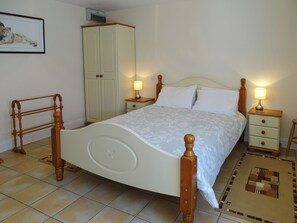 A bedroom with a bed, wooden headboard, bedside tables with lamps, a wardrobe, and a framed picture on the wall.