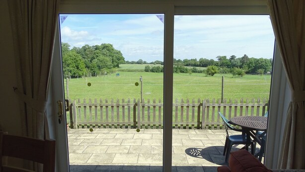 A room with a sliding glass door leading to an outdoor patio with a wooden fence, a table, and a chair. - 2 bedroom accommodation in Leiston, near Aldeburgh (Leiston, near Aldeburgh)