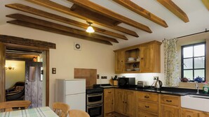 A kitchen with wooden cabinets, a refrigerator, a stove, and a window with curtains. - 2 bedroom accommodation in Hathersage (Hathersage)