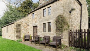 A stone building with a wooden fence, a garden, and outdoor seating. - 2 bedroom accommodation in Hathersage (Hathersage)