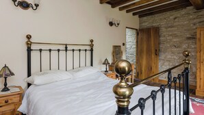 A bedroom with a bed, wooden headboard, stone wall, and a staircase with a balustrade. - 2 bedroom accommodation in Hathersage (Hathersage)