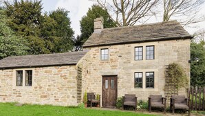 A stone house with a wooden door, two windows, and a small porch with wooden benches. - 2 bedroom accommodation in Hathersage (Hathersage)