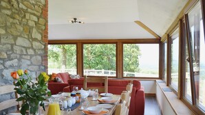 A dining area with a long table set for breakfast, a stone wall, and a view of greenery through large windows. - 3 bedroom accommodation in near Llanwrthwl, Powys (near Llanwrthwl, Powys)