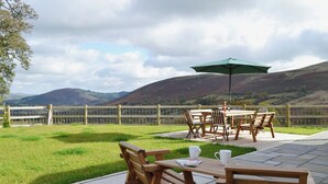 An outdoor patio with wooden furniture and a table, a green umbrella, and a view of hills in the background. - 3 bedroom accommodation in near Llanwrthwl, Powys (near Llanwrthwl, Powys)