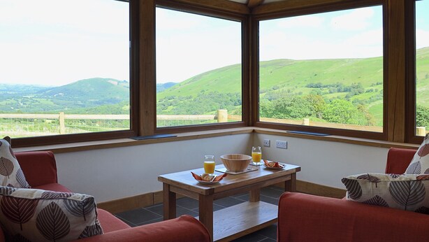A room with a table and chairs, a view of green hills, and a wooden ceiling. - 3 bedroom accommodation in near Llanwrthwl, Powys (near Llanwrthwl, Powys)