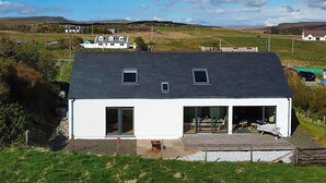 Een modern wit huis met een donker dak, een terras en uitzicht op het omliggende landschap.