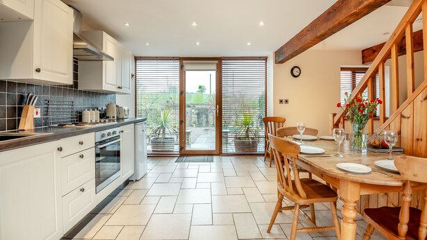 A modern kitchen with white cabinets, a black countertop, and a dining area with wooden chairs and a table set for two. - 2 bedroom accommodation in Bream, near Lydney (Bream, near Lydney)