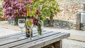 A wooden picnic table with a bottle of wine, two wine glasses, and a vase with flowers. - 2 bedroom accommodation in Bream, near Lydney (Bream, near Lydney)