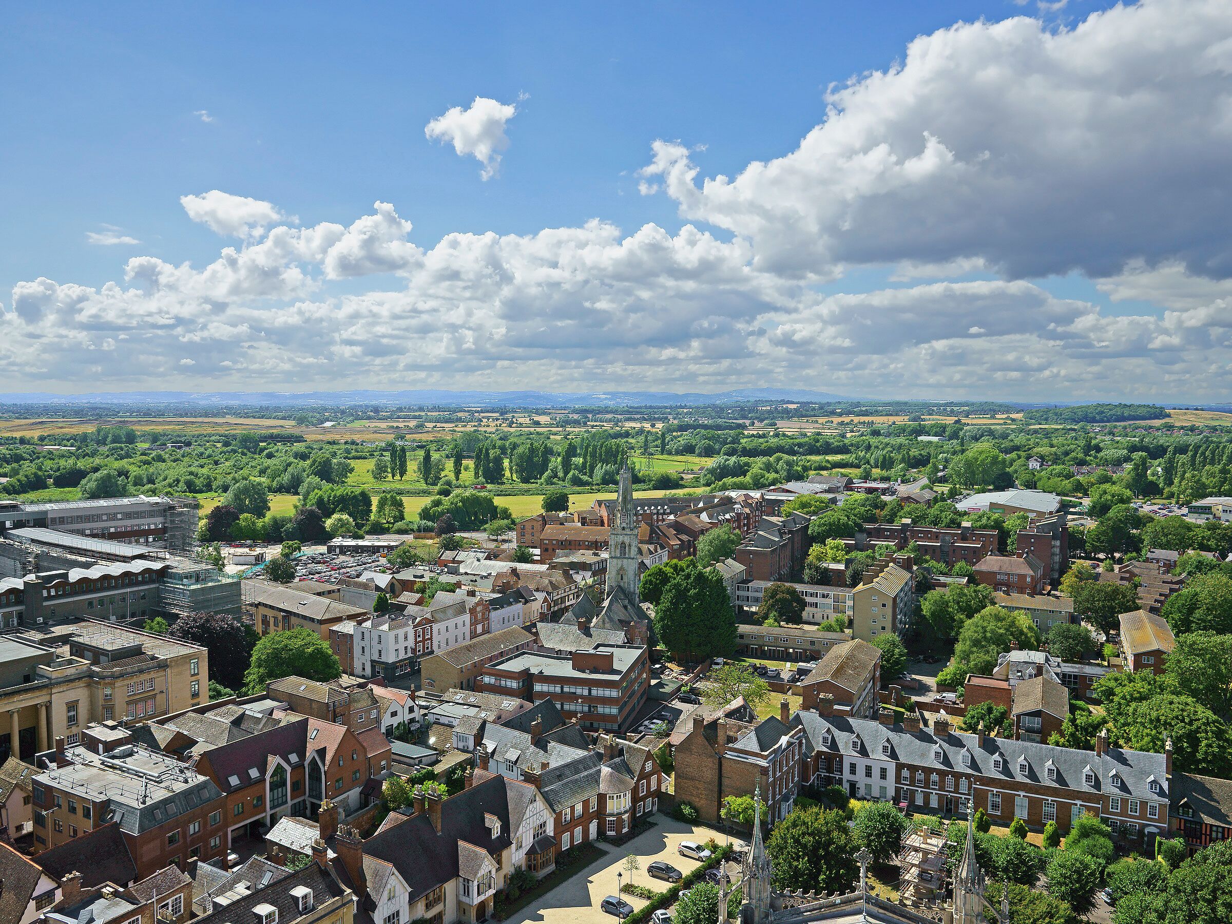 A historic town with dense architecture, including a prominent church spire, surrounded by green fields and a clear sky.