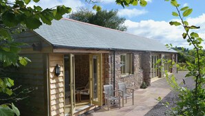 A stone cottage with a tiled patio and a wooden door. - 3 bedroom accommodation in Waterrow, near Wiveliscombe (Waterrow, near Wiveliscombe)