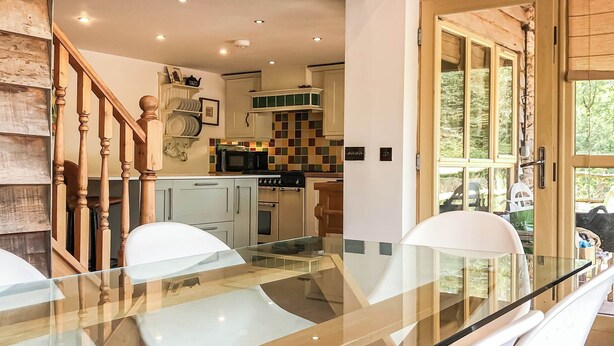 A modern kitchen with white cabinets, a microwave, and a stove. There is a glass dining table with white chairs. - 3 bedroom accommodation in Waterrow, near Wiveliscombe (Waterrow, near Wiveliscombe)