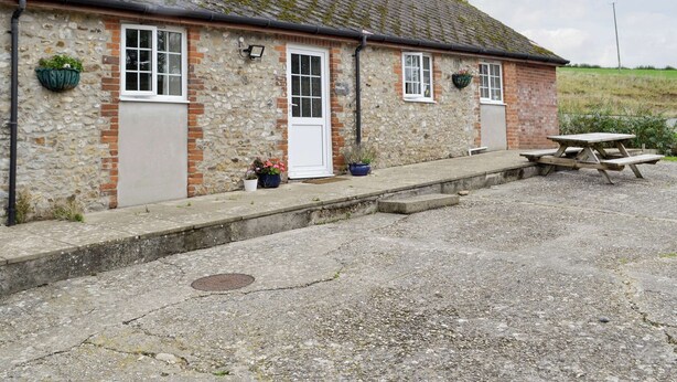 A stone building with a tiled roof, a door, and a window. There is a bench and a planter with flowers. - 2 bedroom accommodation in Wootton Fitzpaine, near Charmouth (Wootton Fitzpaine, near Charmouth)