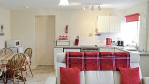 A living room with a white sofa, red pillows, and a plaid blanket. There is a dining area with a table and chairs, and a kitchen with white cabinets and appliances. - 2 bedroom accommodation in Wootton Fitzpaine, near Charmouth (Wootton Fitzpaine, near Charmouth)