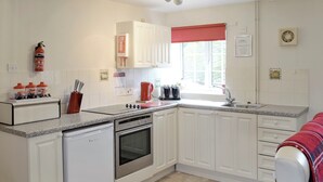 A modern kitchen with white cabinets, a built-in oven, a dishwasher, and a window with a red blind. - 2 bedroom accommodation in Wootton Fitzpaine, near Charmouth (Wootton Fitzpaine, near Charmouth)