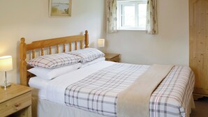 A neatly made bed with a plaid bedspread and pillows, a wooden headboard, a bedside table with a lamp, a window with curtains, and a wooden wardrobe. - 2 bedroom accommodation in Wootton Fitzpaine, near Charmouth (Wootton Fitzpaine, near Charmouth)