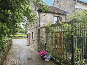 Un bâtiment en pierre avec un chemin pavé menant à une entrée fermée par un portail.