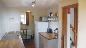 Cocina compacta con microondas, tostadora y tetera sobre la encimera, refrigerador y comedor con mesa y sillas.