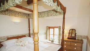 Una cama con dosel y cortinas de estampado floral, un aparador de madera con espejo y una ventana con cortinas.
