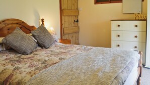 Una camera da letto con testiera in legno, un letto con biancheria da letto floreale, un comodino con una lampada, una porta in legno e un comò con cassetti.