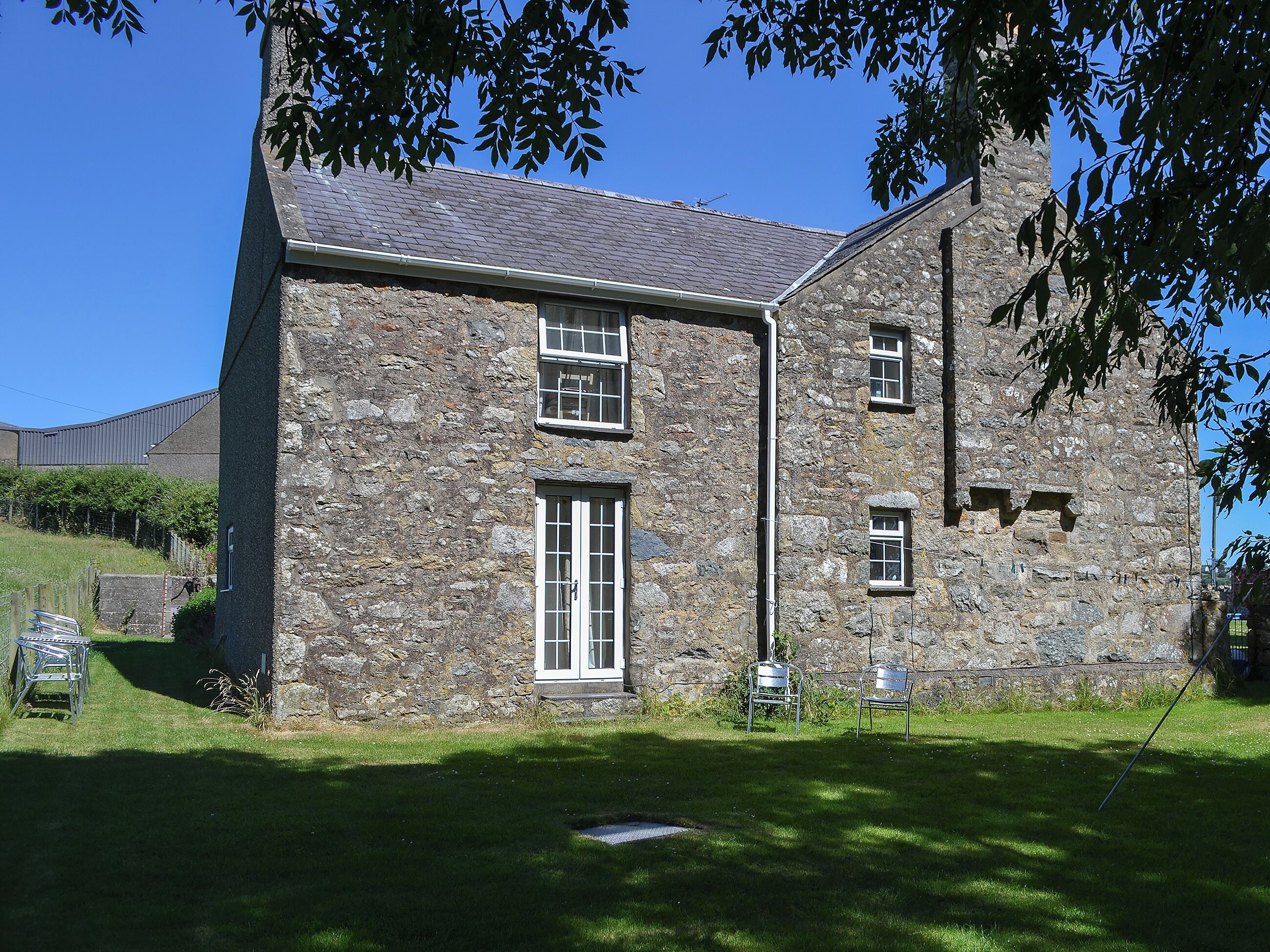 A stone building with a sloped roof, a central door, and two windows on the upper floor.