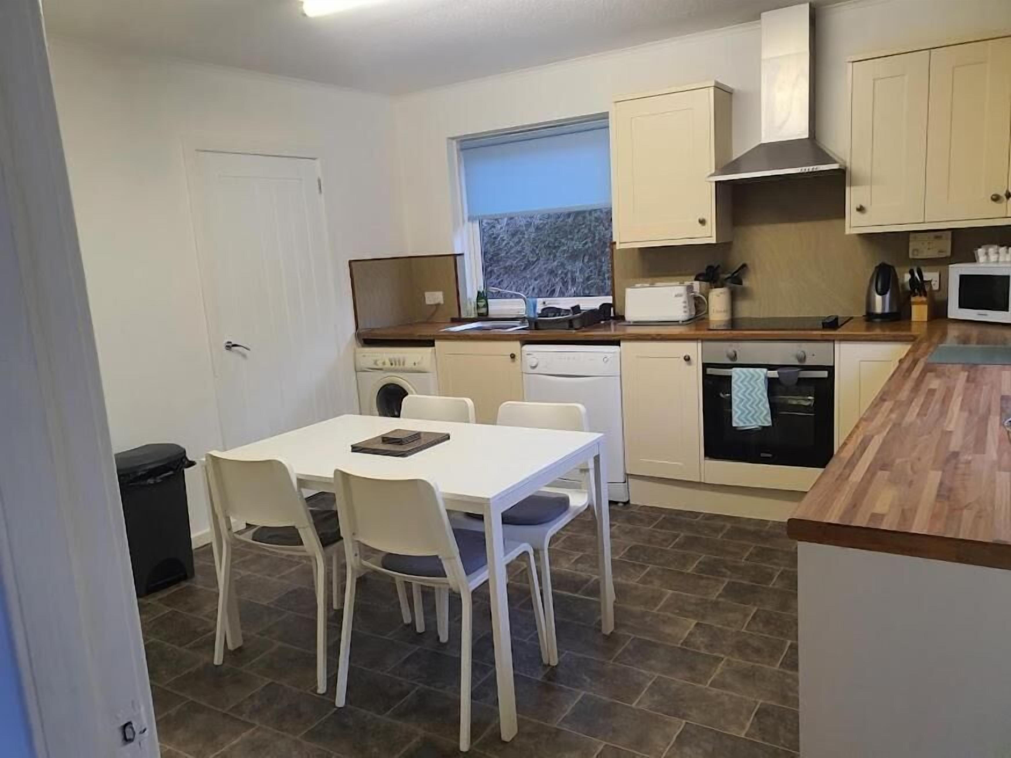 A compact kitchen with a dining table, chairs, a washing machine, a microwave, and a window with a view.