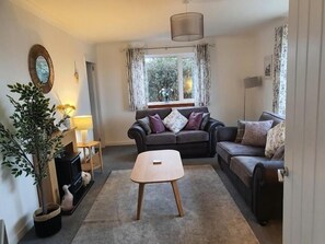 A living room with two sofas, a coffee table, a lamp, a plant, and a window with curtains. - Tigh Na Fraoch, (Skeabost)