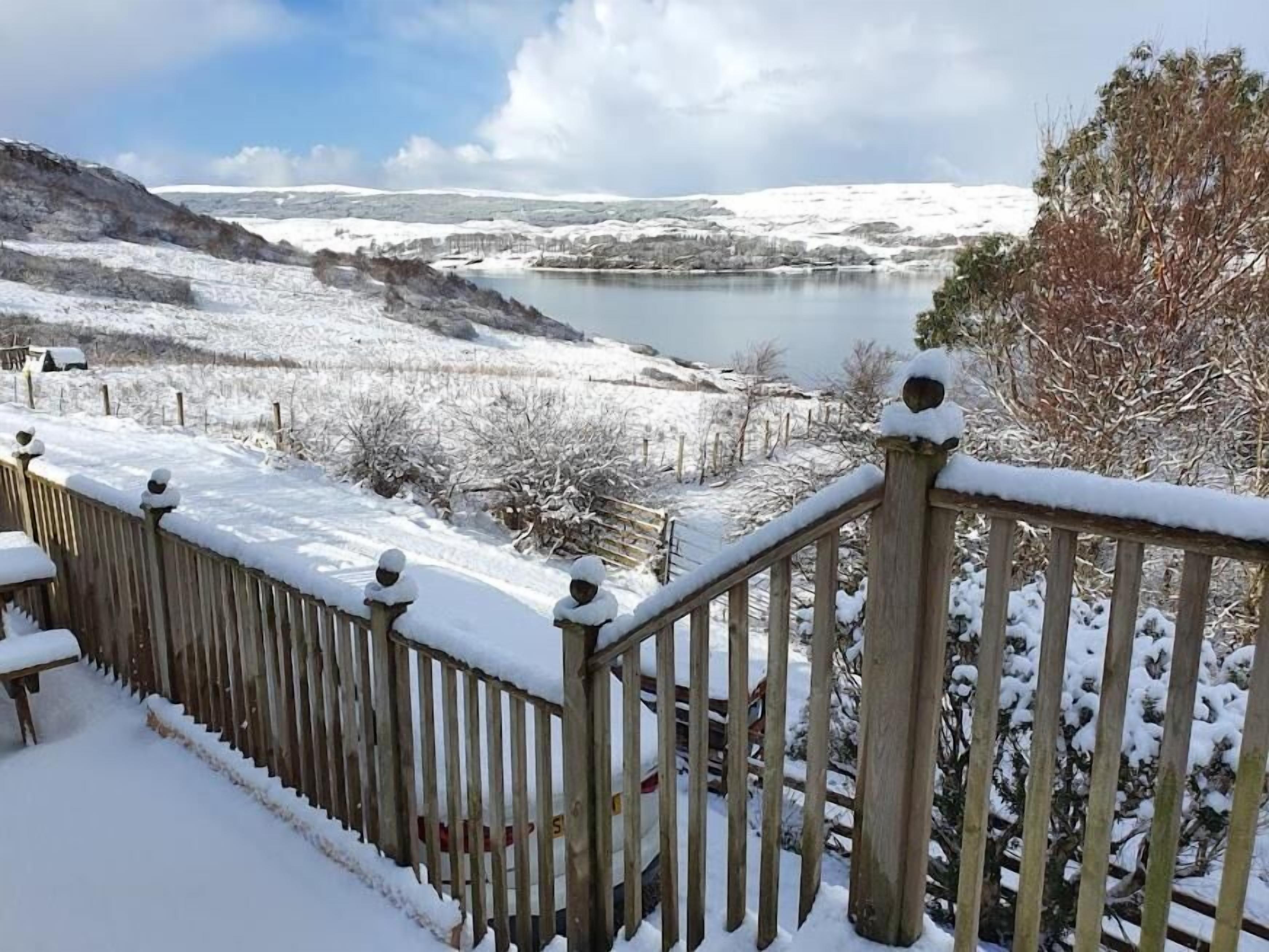 A snow-covered outdoor area with a wooden railing and a view of a lake.