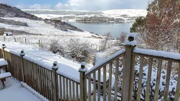 A snow-covered outdoor area with a wooden railing and a view of a lake.