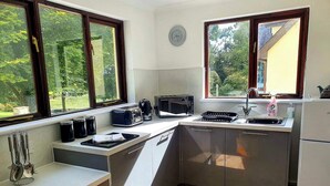 A compact kitchen with a microwave, toaster, and sink. There are windows providing natural light and a view of greenery outside. - Rosecraddoc Manor - Riverbank (Near Liskeard)