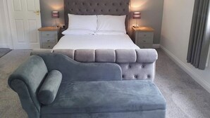 A bedroom with a large bed, two bedside tables, a nightstand, and a grey upholstered chair. - Rosecraddoc Manor - Riverbank (Near Liskeard)