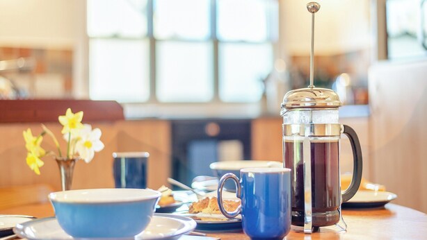 A breakfast table with a coffee press, a blue mug, and a bowl. - HOLLOW CREEK COTTAGE - 28012 (Kirkandrews-on-Eden, near Carlisle)
