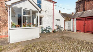 A white building with a bay window, a red door, and a cobblestone courtyard. - HOLLOW CREEK COTTAGE - 28012 (Kirkandrews-on-Eden, near Carlisle)