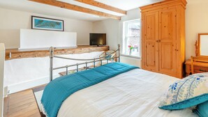 A bedroom with a bed, wooden beams, a TV, a window with flowers, and a wooden wardrobe. - HOLLOW CREEK COTTAGE - 28012 (Kirkandrews-on-Eden, near Carlisle)