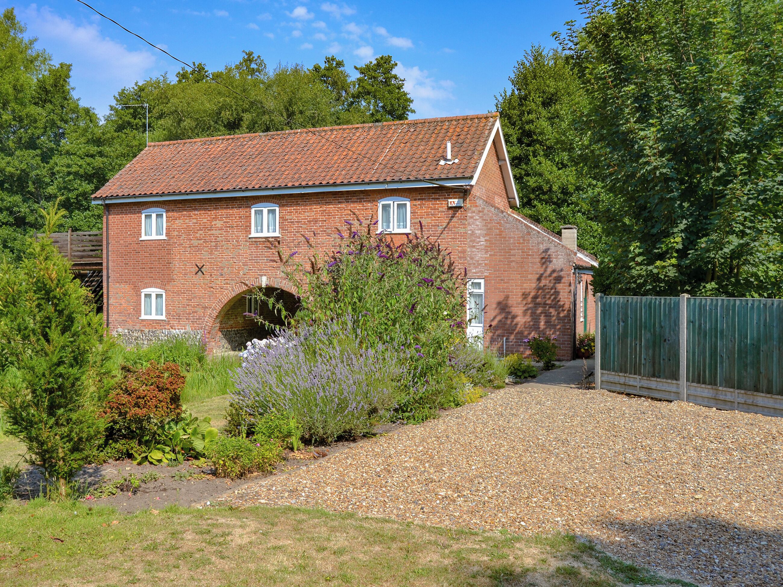 A red brick house with a tiled roof, a small arched entrance, and a gravel driveway.