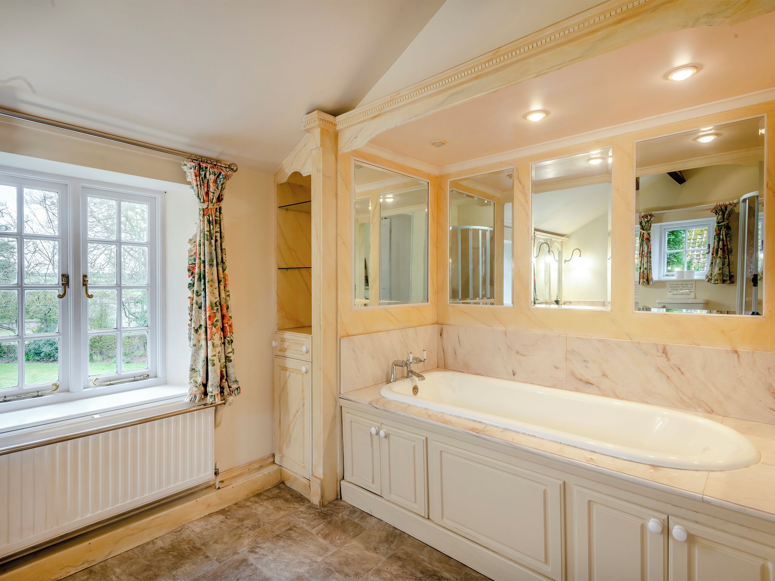 A bathroom with a large bathtub, a window with curtains, and a mirror above the sink.