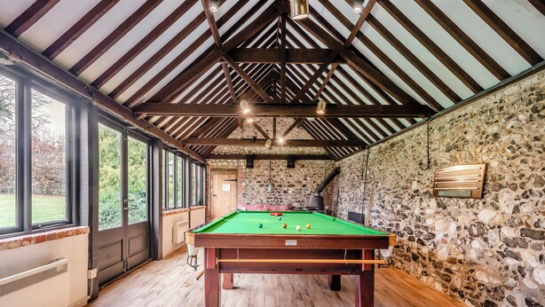 A pool table in a room with stone walls and wooden beams, large windows, and a stone fireplace. - 6 bedroom accommodation in Fring, near Kings Lynn (Fring, near Kings Lynn)