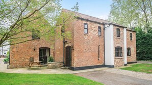 A brick building with a traditional design, featuring a wooden bench outside, a paved pathway, and a grassy area.
