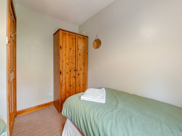 A bedroom with a green bed, a wooden wardrobe, and a striped carpet.
