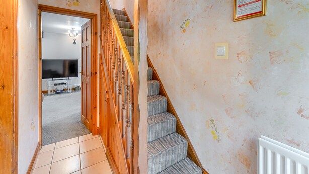Ein Flur mit einer Holztreppe, einem an der Wand befestigten Brandschutznachricht und einem gefliesten Boden.