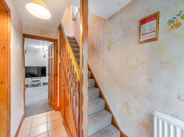 A hallway with a wooden staircase, a wall-mounted fire safety sign, and a tiled floor.