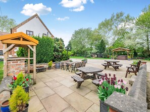 A patio area with wooden tables and benches, surrounded by potted plants and a brick structure. - 3 bedroom accommodation in York (York)