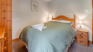 Ein ordentlich bezogenes Bett mit einem hölzernen Kopfteil, einer Nachttischlampe und einem kleinen Nachttisch mit Schubladen.