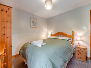 A neatly made bed with a wooden headboard, a bedside lamp, and a small wooden nightstand with drawers.