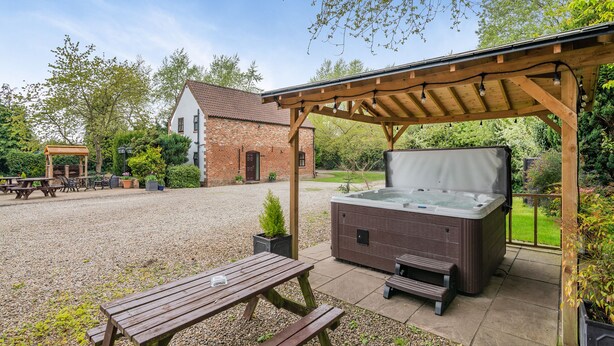 A patio area with a hot tub, wooden benches, and a pergola structure.