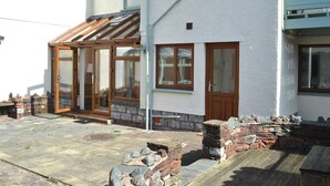 Une maison à deux étages avec une façade en pierre, des portes en bois et une véranda dotée de portes vitrées.