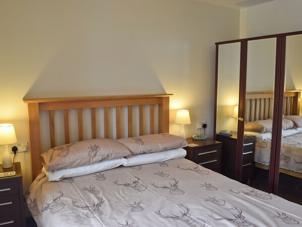 Un dormitorio con cama, mesitas de noche, un espejo y un velador.
