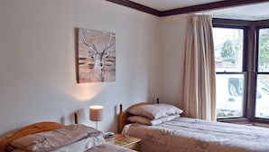 Une chambre avec deux lits, une table de chevet avec une lampe, un tableau au mur et une fenêtre avec des rideaux.