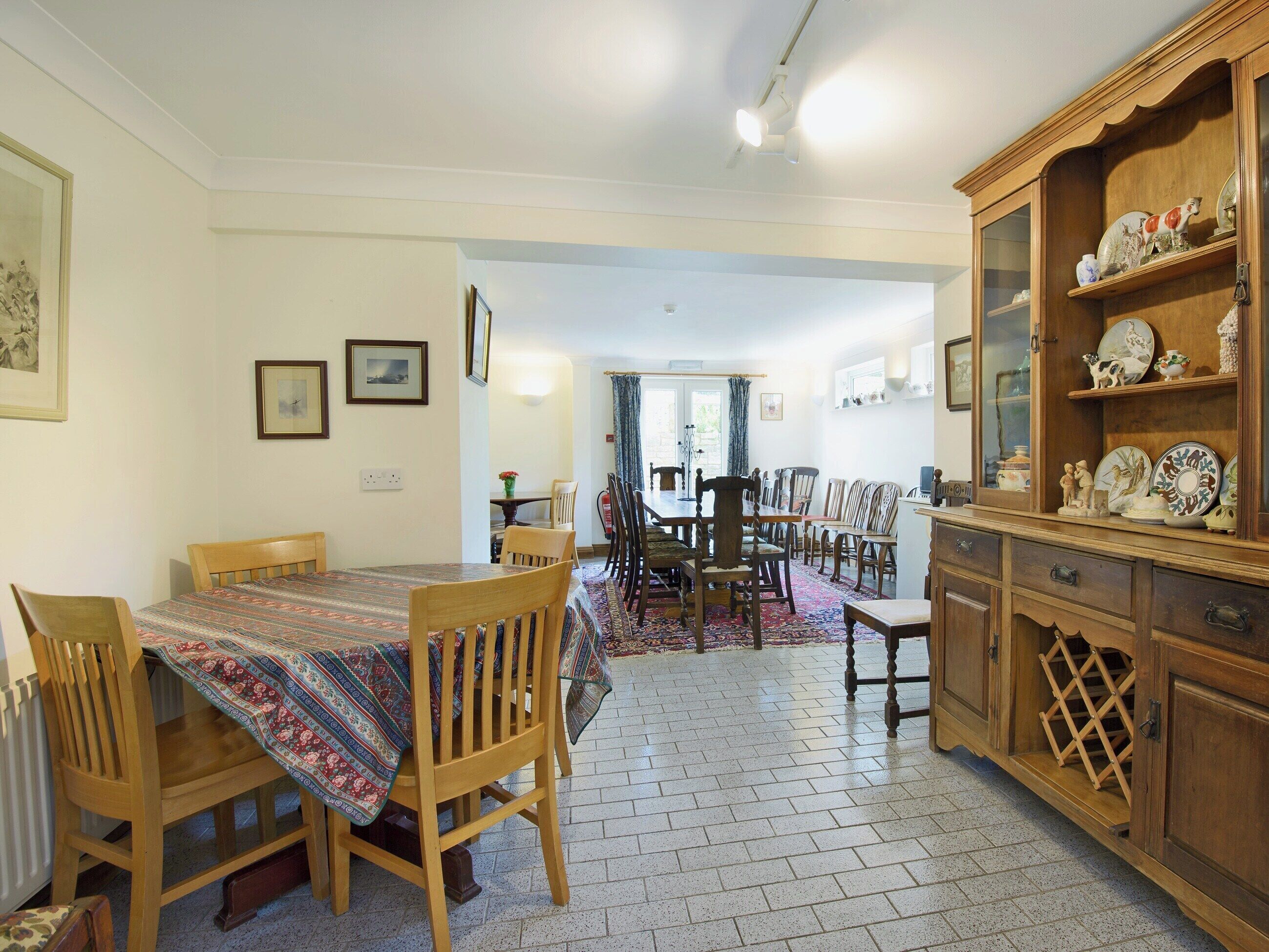 A dining area with a wooden table and chairs, a patterned tablecloth, and a cabinet with decorative plates.