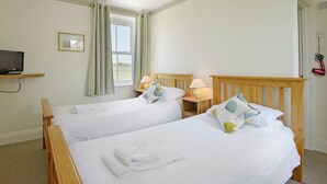 A hotel room with two single beds, a TV on a shelf, a bedside table with a lamp, and a window with curtains. - 7 bedroom accommodation in Acton, near Langton Matravers (Acton, near Langton Matravers)